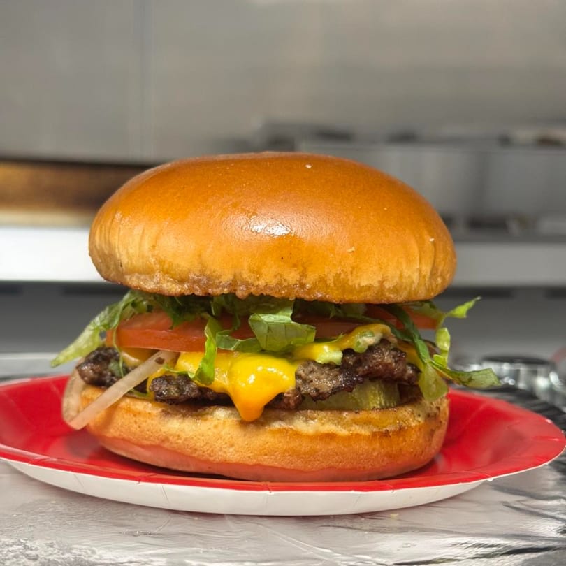 A double cheeseburger with melted cheese, lettuce, tomato, and onions on a red paper plate.
