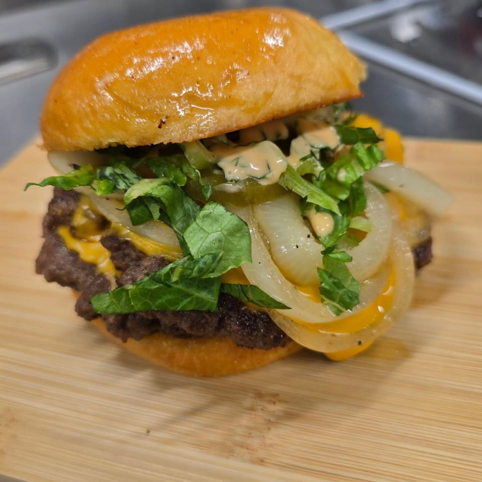A juicy double cheeseburger with melted cheese, fresh lettuce, onions, and special sauce on a wooden board.