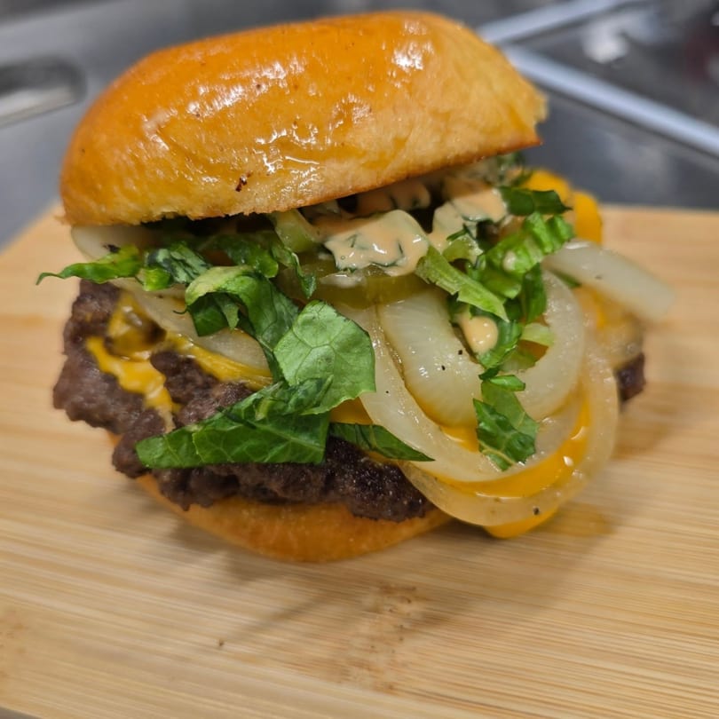 A juicy double cheeseburger with melted cheese, fresh lettuce, onions, and special sauce on a wooden board.